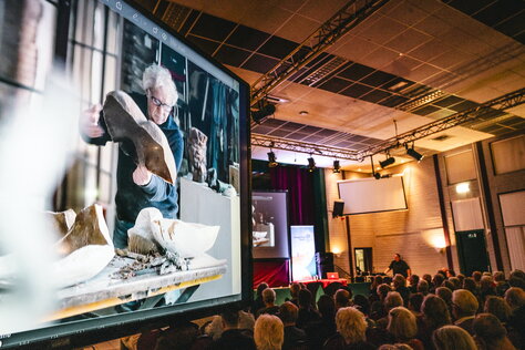 Groot scherm met daarop de video met enkele omwonenden tijdens de bewonersavond Meerssen